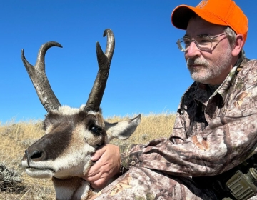 A hunter in camouflage gear kneels beside their harvested antelope, showcasing the animal's impressive antlers and strong build, a testament to a rewarding hunt with SNS.